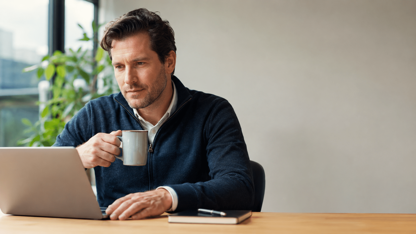 Nederlandse professional zit nadenkend aan een modern bureau met laptop en koffiemok in een rustige, lichte werkomgeving.