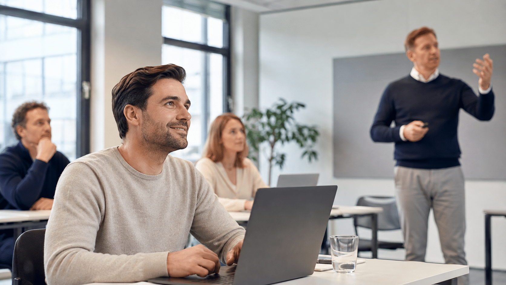 Tevreden cursist volgt een Copilot-training op een laptop in een rustig, professioneel klaslokaal terwijl een docent uitleg geeft.