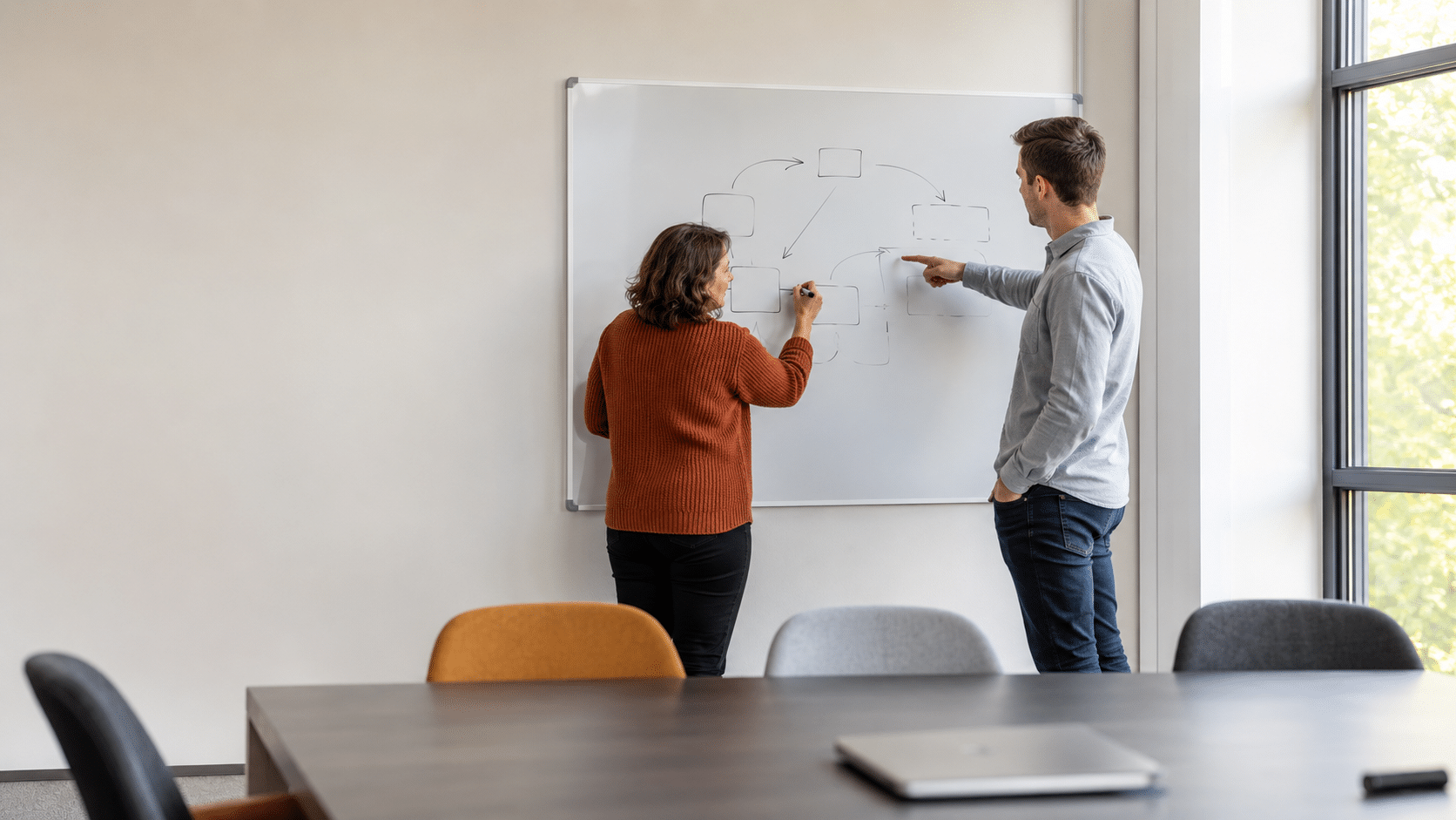 Trainer en deelnemer schetsen samen een integratieschema op een whiteboard in een trainingsruimte.