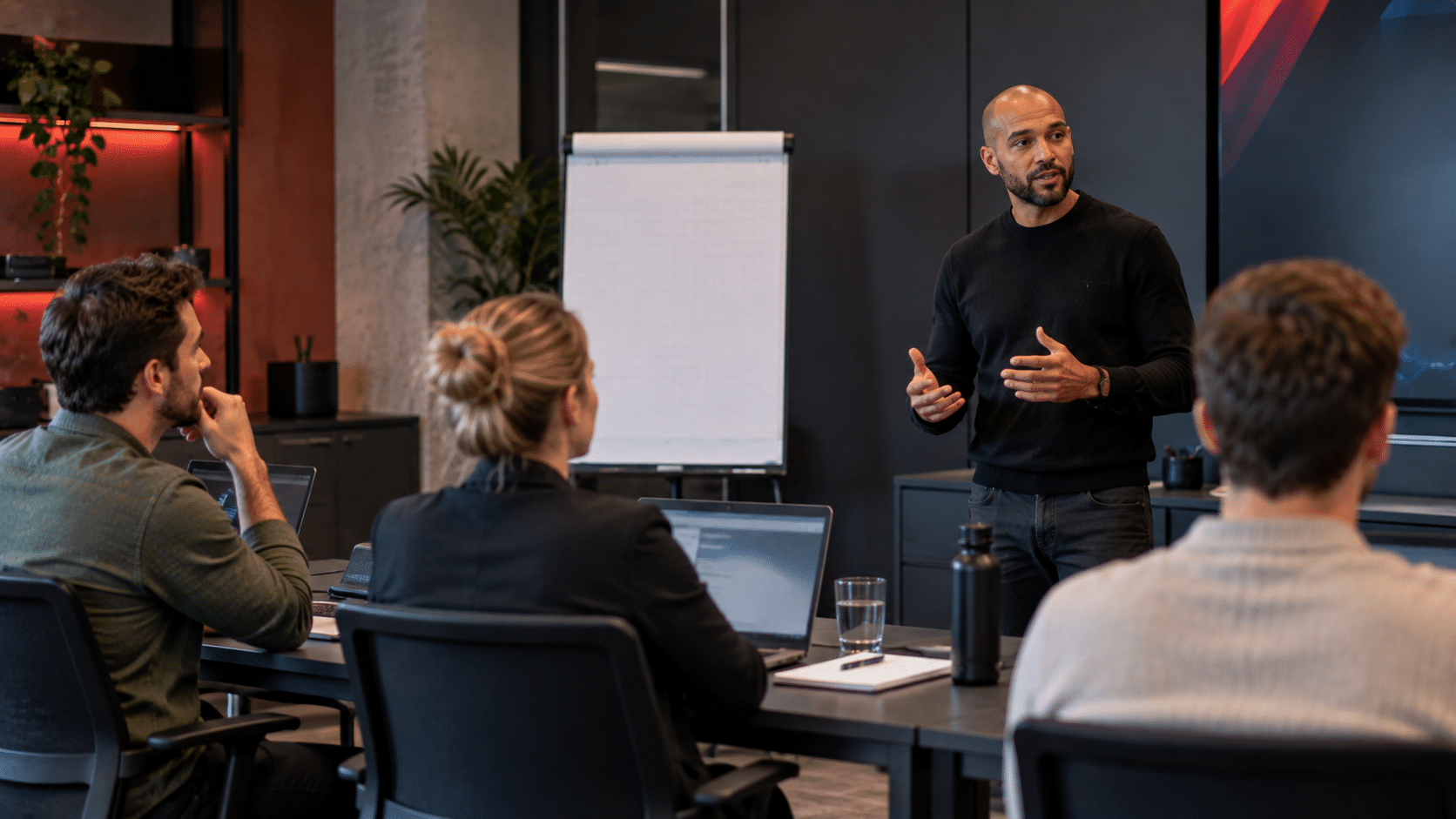 Trainer geeft een EC-Council-cybersecuritytraining aan drie deelnemers in een moderne, donkere trainingsruimte met laptops.
